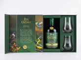 Estuche verde de lujo abierto de Ron Viejo de Caldas Gran Reserva Especial. Contiene una botella, dos copas de cristal grabadas y una tapa interior decorada con texto y coloridas ilustraciones de aves sobre fondo blanco.