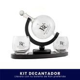 Set de bar que incluye un decantador de vidrio esférico montado sobre un soporte giratorio y dos vasos de cristal, todos con el logo de Ron Viejo de Caldas grabado, sobre fondo blanco. En la parte inferior tiene un banner azul con el texto "Kit Decantador Llévalo con tu botella de Ron preferida".