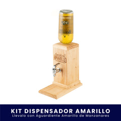 Dispensador de madera para licor con grifo metálico, diseñado para sostener una botella invertida de Aguardiente Amarillo de Manzanares. Incluye el logo de la marca grabado en la madera y descansa sobre una base plana, todo sobre un fondo blanco. En la parte inferior tiene un banner azul con el texto "Kit Dispensador Amarillo Llévalo con Aguardiente Amarillo de Manzanares".