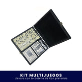 Estuche negro abierto que contiene un kit de juegos de mesa con fichas de dominó, dados y una baraja de cartas sobre fondo blanco. En la parte inferior tiene un banner azul con el texto "Kit Multijuegos Llévalo con tu botella de Ron preferida