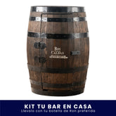 Barril de madera modificado como gabinete para mini bar, con aros metálicos oscuros, bisagras y pasador. Tiene grabado el logo de Ron Viejo de Caldas en la puerta frontal, sobre fondo blanco. En la parte inferior tiene un banner azul con el texto "Kit Tu Bar en Casa Llévalo con tu botella de Ron preferida