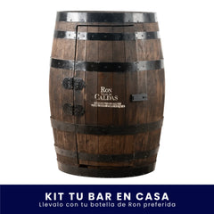 Barril de madera modificado como gabinete para mini bar, con aros metálicos oscuros, bisagras y pasador. Tiene grabado el logo de Ron Viejo de Caldas en la puerta frontal, sobre fondo blanco. En la parte inferior tiene un banner azul con el texto "Kit Tu Bar en Casa Llévalo con tu botella de Ron preferida