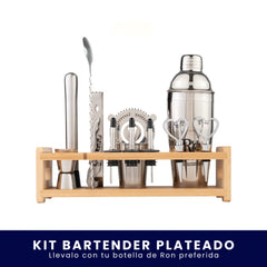 Set de coctelería plateado organizado en una base de madera. Incluye coctelera, medidor, cuchara mezcladora, macerador, colador y dosificadores sobre fondo blanco. En la parte inferior tiene un banner azul con el texto "Kit Bartender Plateado Llévalo con tu botella de Ron preferida".