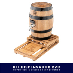Dispensador de madera en forma de barril con aros negros y grifo metálico, montado sobre una base de madera tipo estiba (pallet) con el logo grabado de Ron Viejo de Caldas, sobre fondo blanco. En la parte inferior tiene un banner azul con el texto "Kit Dispensador RVC Llévalo con tu botella de Ron preferida".