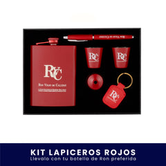 Set de regalo en caja negra que incluye una licorera de bolsillo roja, dos vasos tipo shot rojos, un lapicero, un embudo y un llavero, todos con el logo de Ron Viejo de Caldas, sobre fondo blanco. En la parte inferior tiene un banner azul con el texto "Kit Lapiceros Rojos Llévalo con tu botella de Ron preferida".