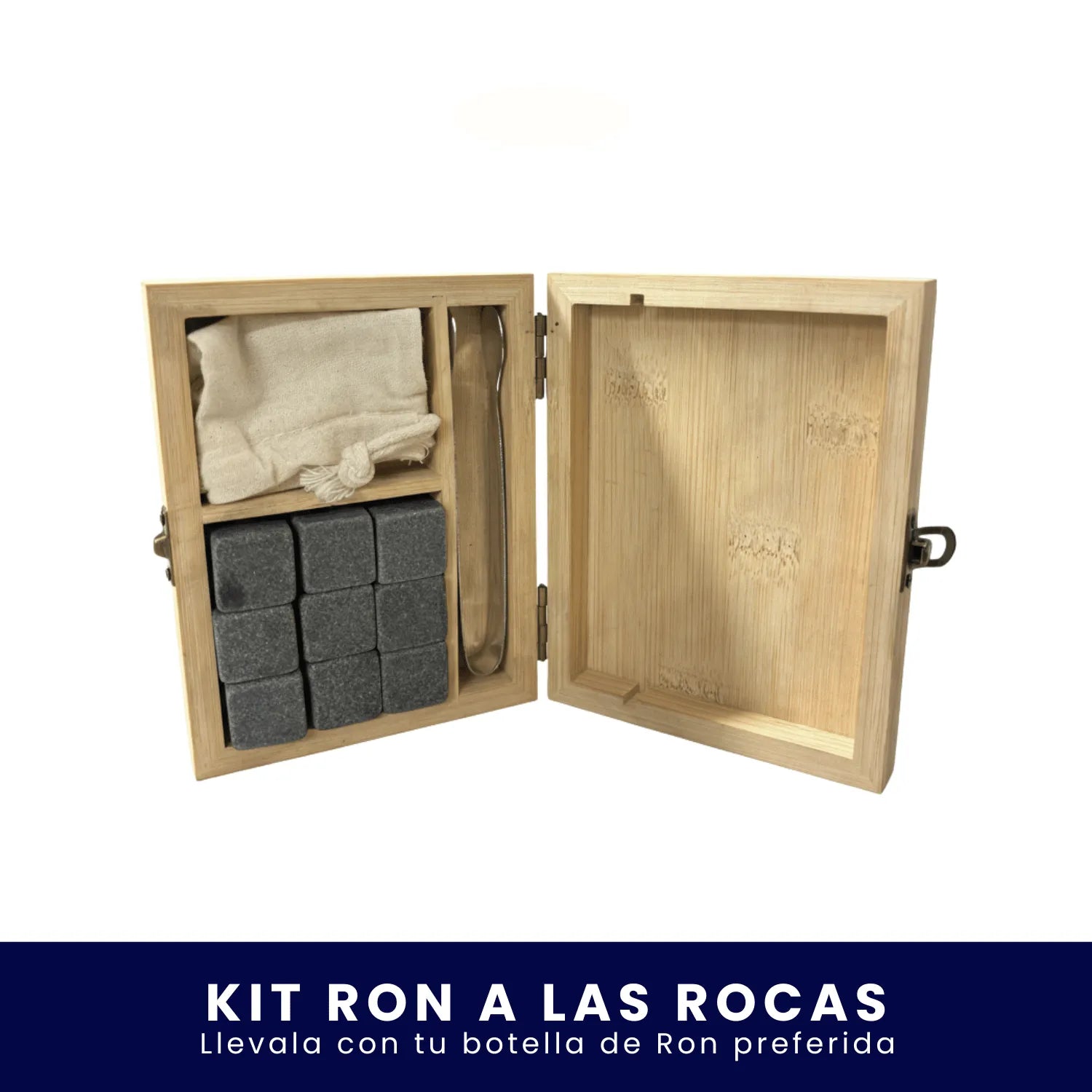 Caja de madera abierta que contiene un kit de piedras enfriadoras para licor, incluyendo cubos de roca, pinzas y una pequeña bolsa de tela, sobre fondo blanco. En la parte inferior tiene un banner azul con el texto "Kit Ron a las Rocas Llévala con tu botella de Ron preferida".