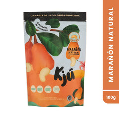 Empaque frontal tipo doypack de Marañón Natural marca Kjú de 100g. Su diseño es en tonos blanco y naranja, destacando ilustraciones de la fruta del marañón, su nuez y follaje, junto al sello de certificación Kosher y el texto "La magia de la Colombia profunda" en la parte superior.
